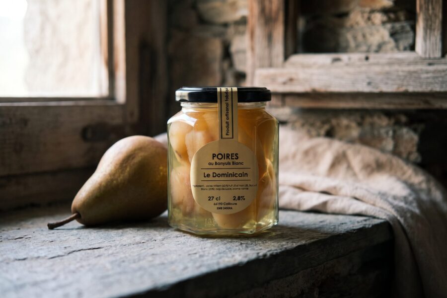 Bocal de poires au Banyuls blanc devant une fenêtre, poire fraîche posée à côté